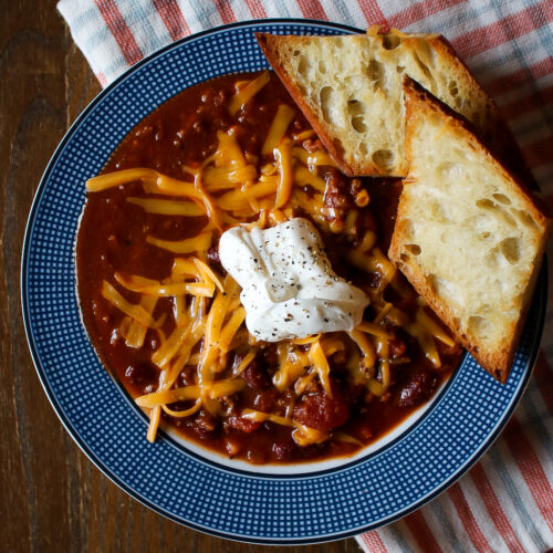easy, tasty chili recipe - bowl of chili topped with shredded cheese, sour cream and buttered toast