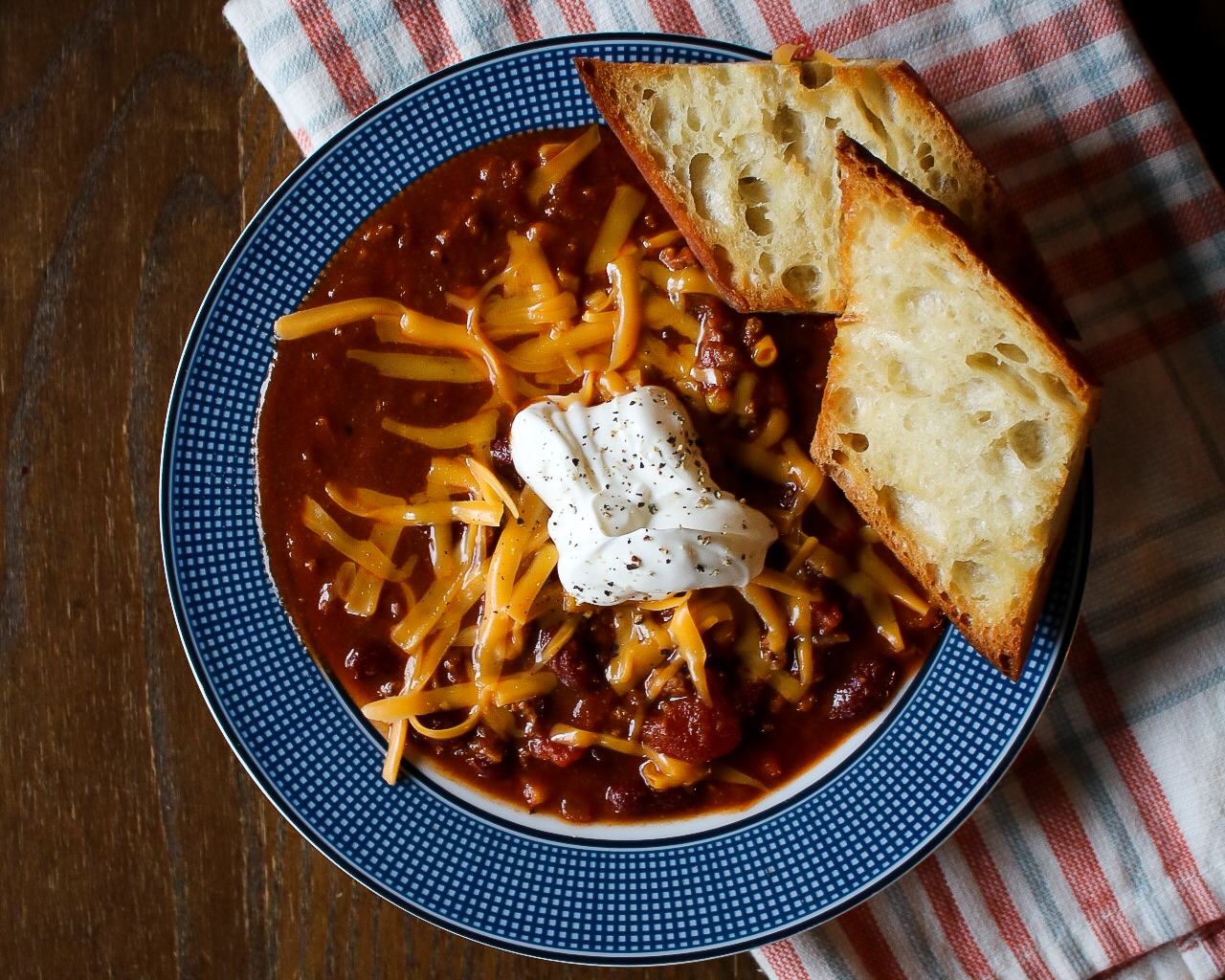 easy, tasty chili recipe - bowl of chili topped with shredded cheese, sour cream and buttered bread.